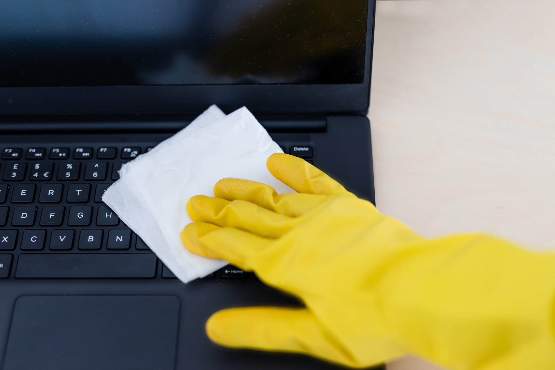 Person in a yellow gloves wiping down a keyboard